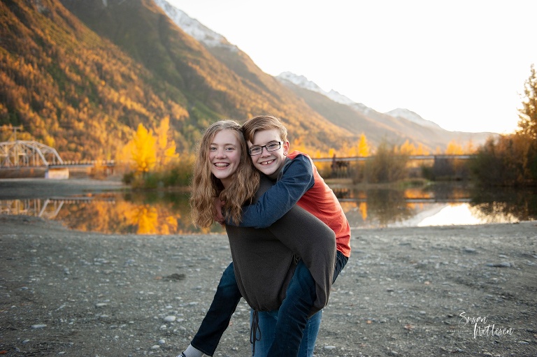 big sister gives brother piggy back ride during family photos in Alaska