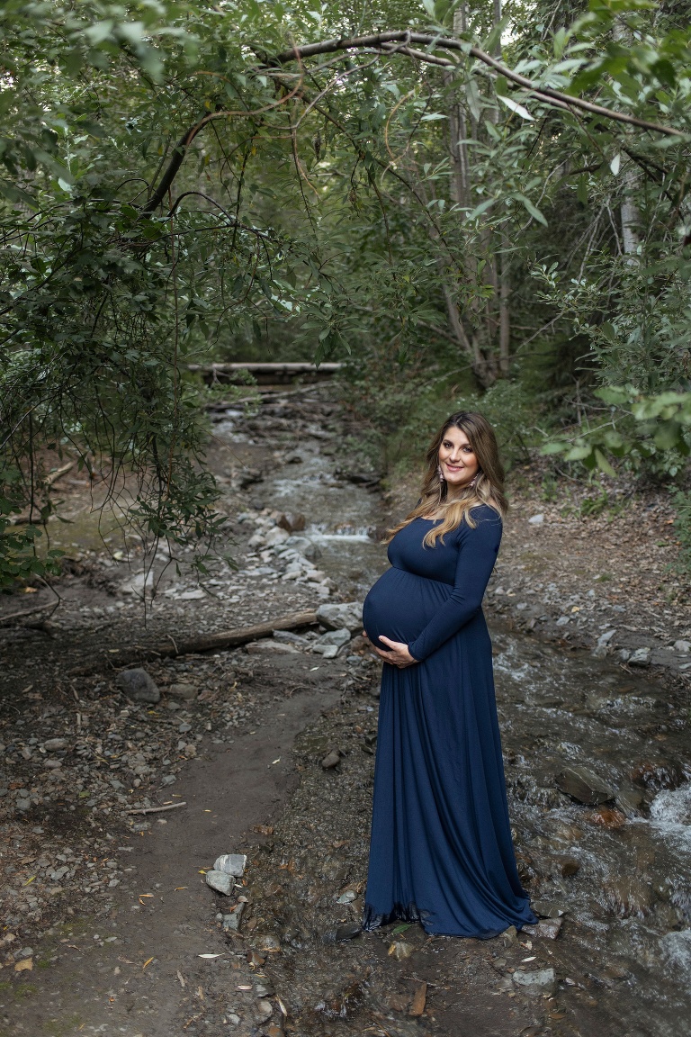 expecting mother holds baby belly wearing navy maternity gown during Eklutna Lake Maternity Portraits