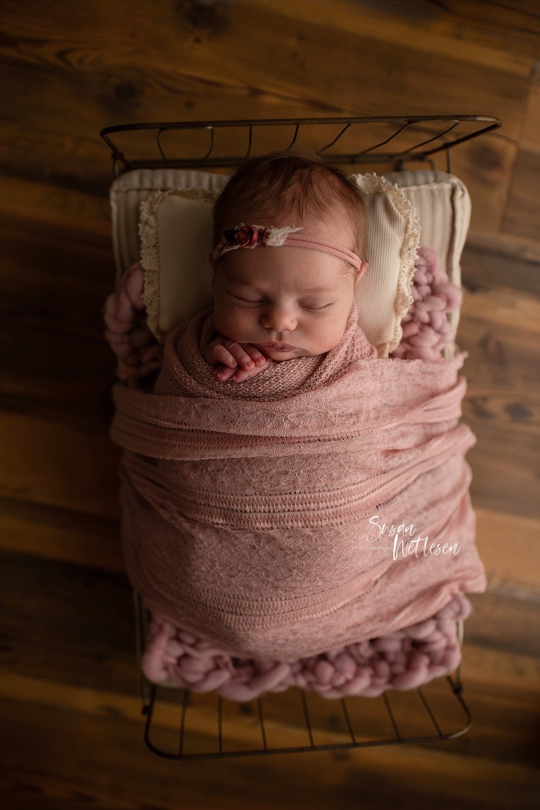 sleeping baby tucked in light pink blanket with pink headband during Alaska Classic Newborn Portrait Session