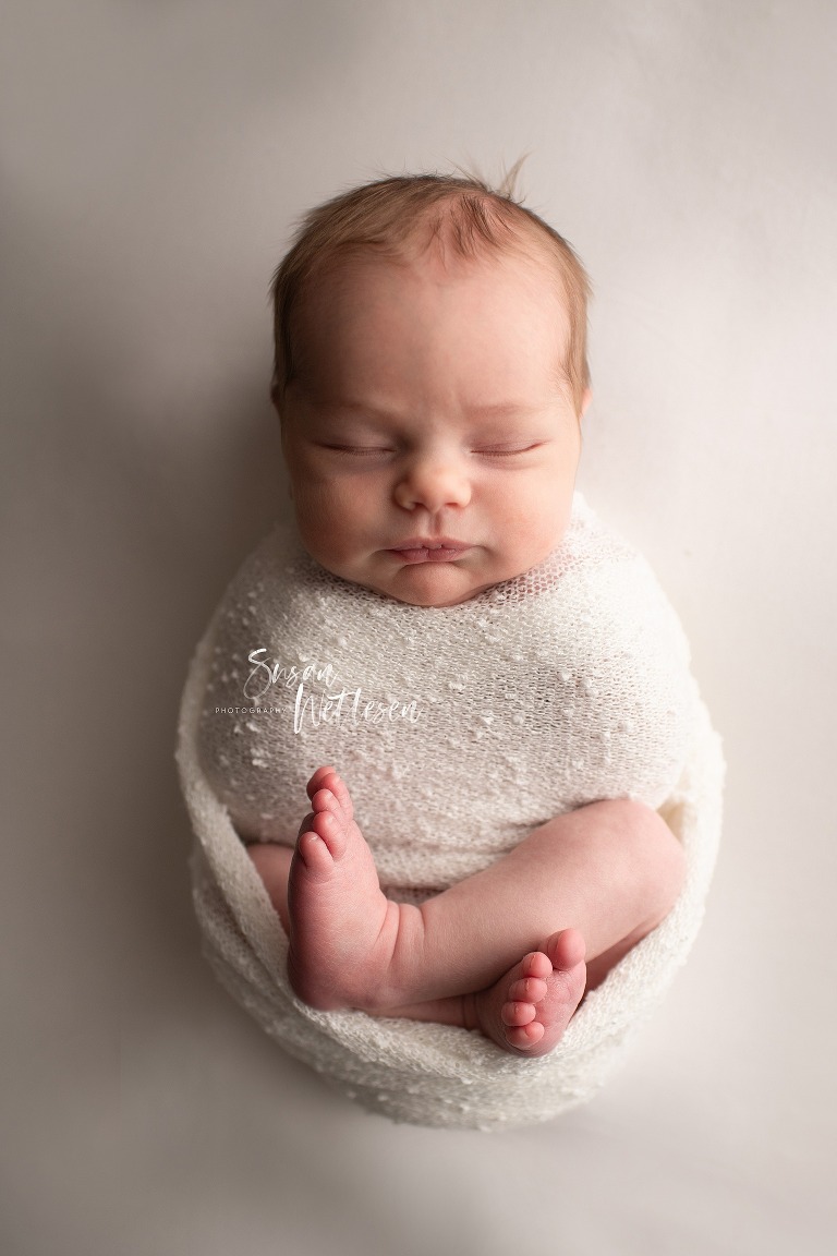 Sleeping newborn wrapped in white blanket with legs out during Alaska Classic Newborn Portrait Session