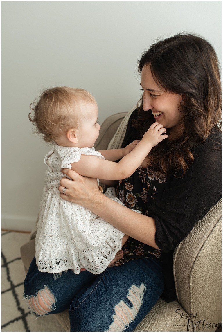 Mom and baby girl face each other and mom smiles down at her