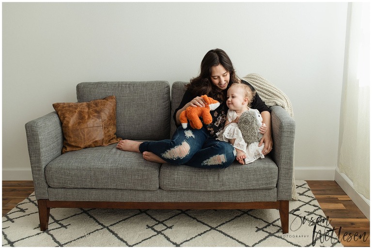 Mom and baby girl cuddle on couch and play with stuffed animals during Alaska Motherhood Session